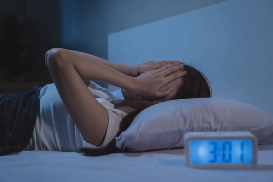 Woman lying awake in bed at night beside an alarm clock